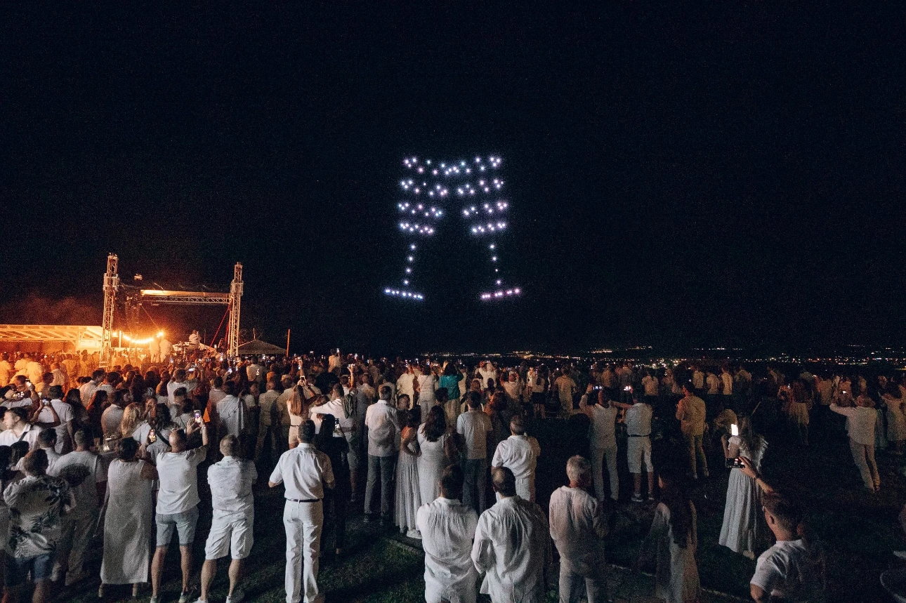 Eine Lichtshow mit Drohnen bei einem Event, es sind Sektgläser in der Luft zu sehen.