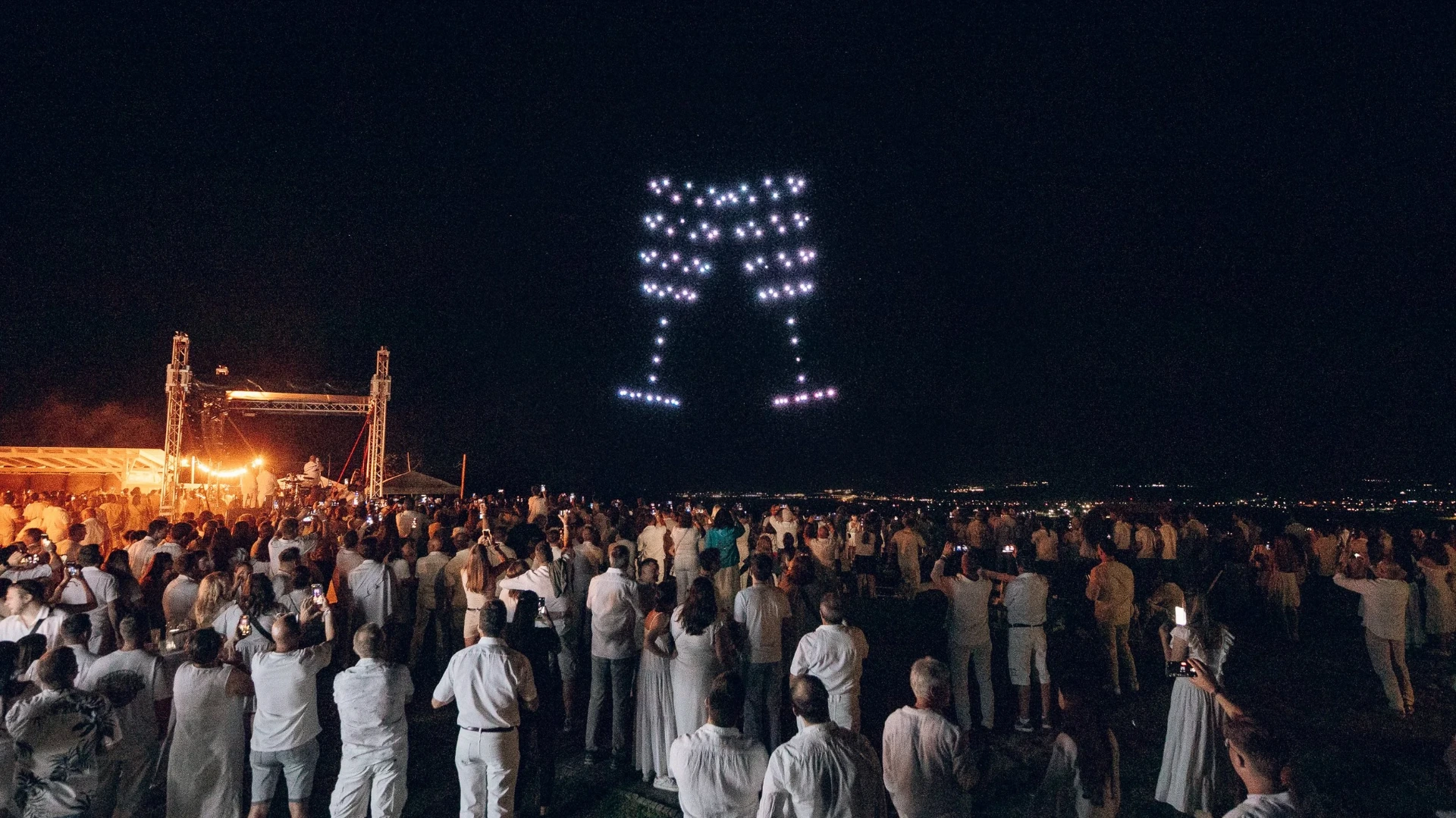 Eine Lichtshow mit Drohnen bei einem Event, es sind Sektgläser in der Luft zu sehen.